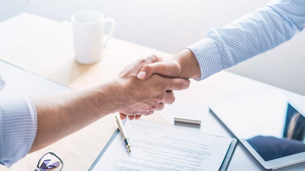 A man and a woman shake hands at the conference table.