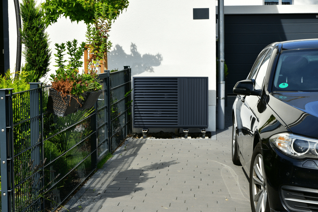 Eine schwarze Wärmepumpe neben dem Eingang zur Garage eines Einfamilienhauses.