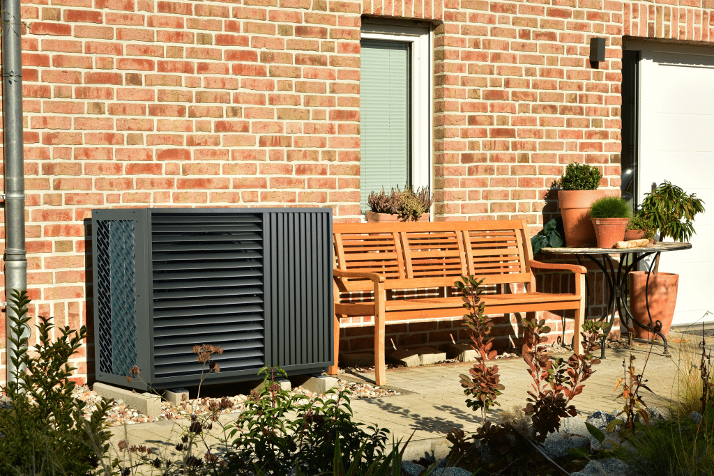 A black heat pump in front of the façade of a detached house.