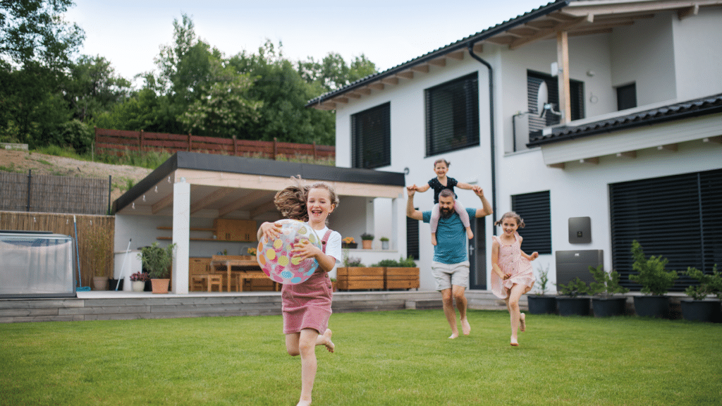 Ein Mann spielt mit seinen drei Kindern im Garten ihres Familienhauses.